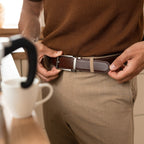 Person adjusting a brown belt with a silver buckle in a casual setting.