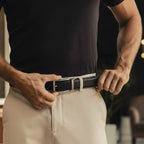 Person adjusting a black belt on beige pants with a blurred background