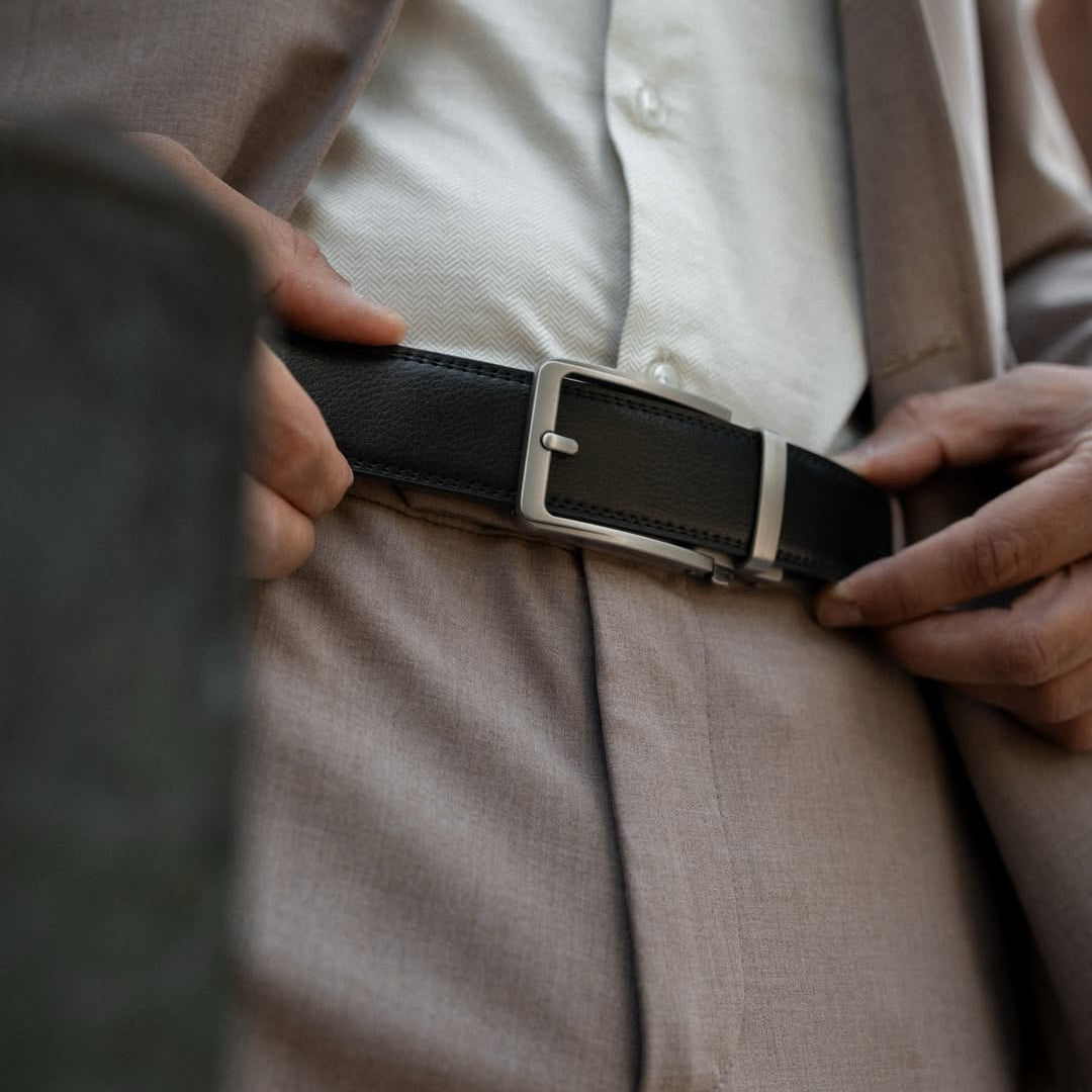 Person adjusting a black belt with a silver buckle on beige pants.