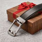 Black leather belt with silver buckle on a wooden box with a red ribbon.